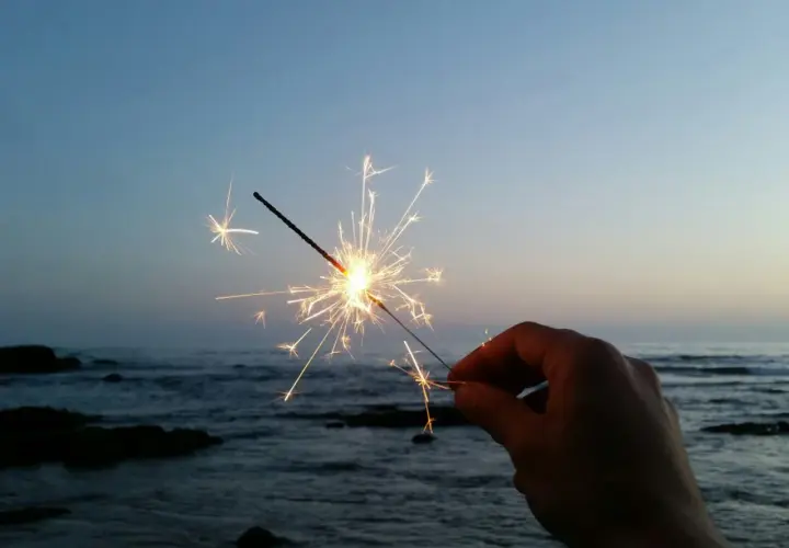 Ein Wunderkerze leuchtet am Silvesterabend am Strand. Die Funken tanzen über dem ruhigen Meer und dem klaren Himmel.