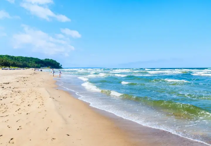Ein sonniger Tag am Ostseebad Baabe. Menschen spazieren am breiten Sandstrand entlang, während die Wellen der Ostsee sanft ans Ufer rollen.