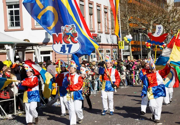 Bunte Kostüme und Fahnen beim Fasching 2026. Menschen feiern ausgelassen in der Stadt.