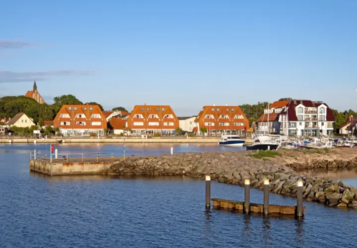 Hafen mit roten Ziegeldächern, Booten und einem Kirchturm im Hintergrund.