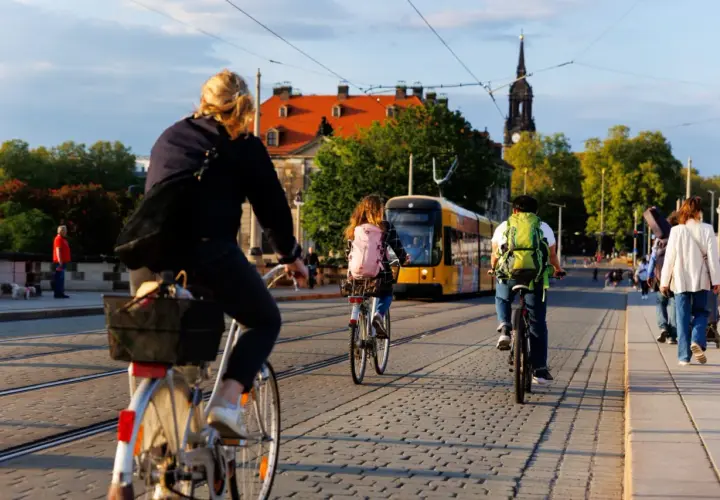 Fahrradfahrer mit Rucksäcken genießen das Bikepacking Deutschland. Eine Straßenbahn fährt vorbei, während Menschen auf Kopfsteinpflaster radeln und gehen.