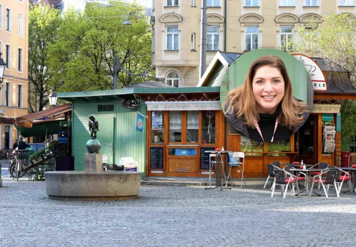 Lächelnde Frau vor einem Stehcafé in Haidhausen. Ein Brunnen und ein kleiner Junge als Statue sind im Vordergrund.