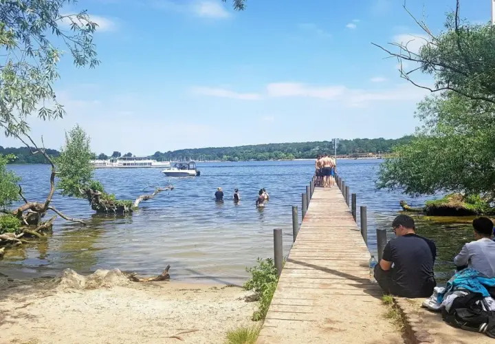 Sommer am ummanz strand: Menschen planschen im Wasser, andere sitzen am Steg. Ein sonniger Tag am See.