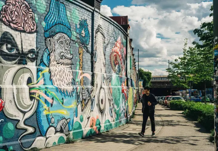 Mann geht an bunter Street Art in München vorbei. Die Wand ist mit fantasievollen Figuren und Mustern bemalt.