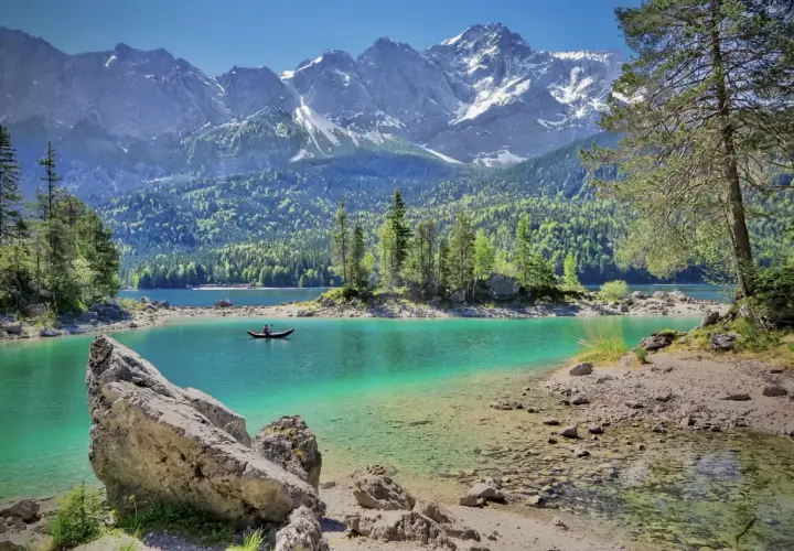 Türkiser Bergsee in Deutschland mit schneebedeckten Gipfeln im Hintergrund. Ein Kanufahrer genießt die Ruhe.