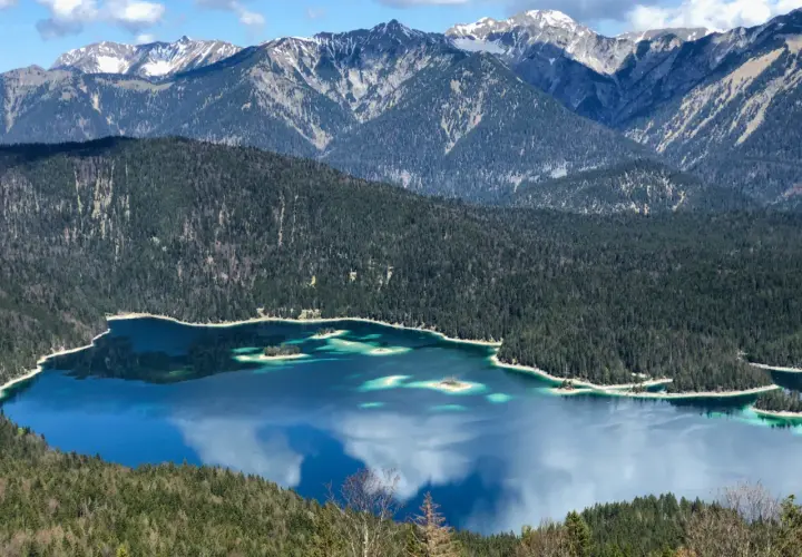 Blick vom Eibsee zur Zugspitze: Türkisblaue Wasserflächen, bewaldete Hänge und schneebedeckte Gipfel. Ein Traumziel für Wanderer.