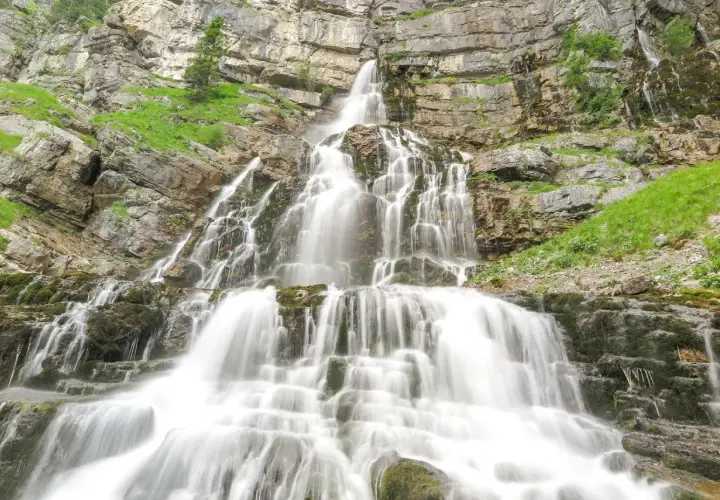 Ein beeindruckender, mehrstufiger murnau wasserfall stürzt über moosbewachsene Felsen in die Tiefe, umgeben von steilen, grünen Hängen.