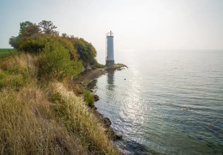 Leuchtturm auf der Halbinsel Zudar, umgeben von üppiger Vegetation und dem glitzernden Meer.
