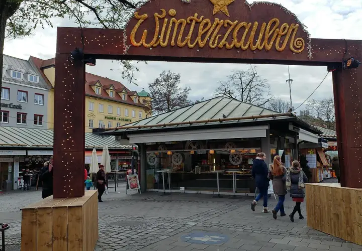 Der Viktualienmarkt zeigt seinen Winterzauber. Menschen schlendern vorbei an Ständen, die auf den Weihnachtsmarkt einstimmen.
