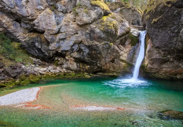 Türkiser bergsee mit einem tosenden wasserfall, der in die klare Tiefe stürzt. Felsen und Moos umrahmen dieses Naturschauspiel.