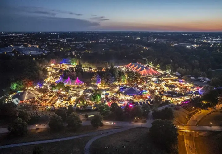 Nachtansicht des beleuchteten Tollwood Festivals im Olympiapark München mit bunten Zelten und Lichtern.