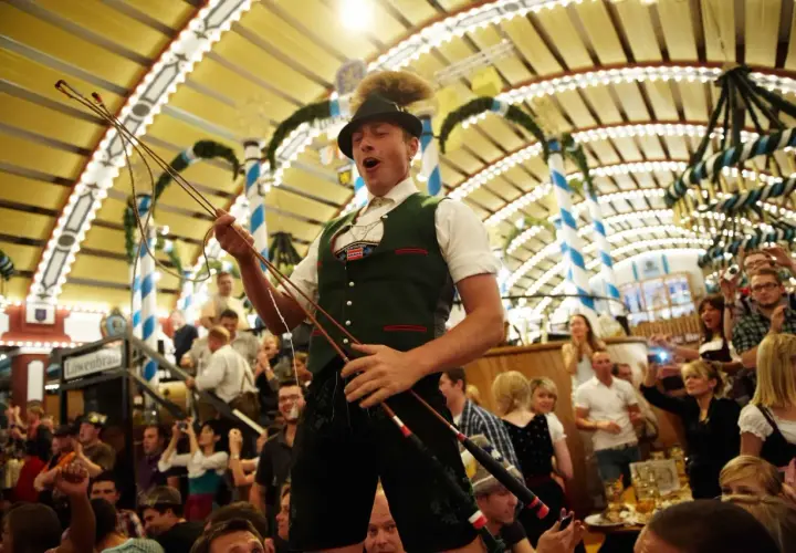 Mann im bierzelt oktoberfest mit Peitsche, jubelnde Menge im Hintergrund.