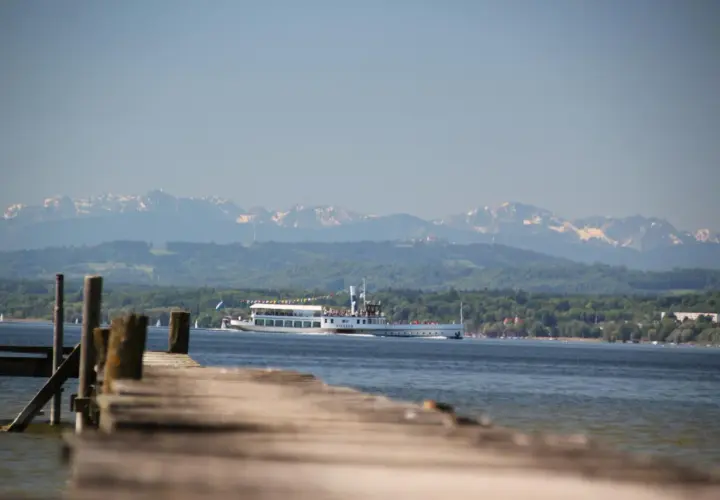 Holzsteg am Ammersee mit einem Ausflugsschiff, im Hintergrund die schneebedeckten Ammersee Berge.