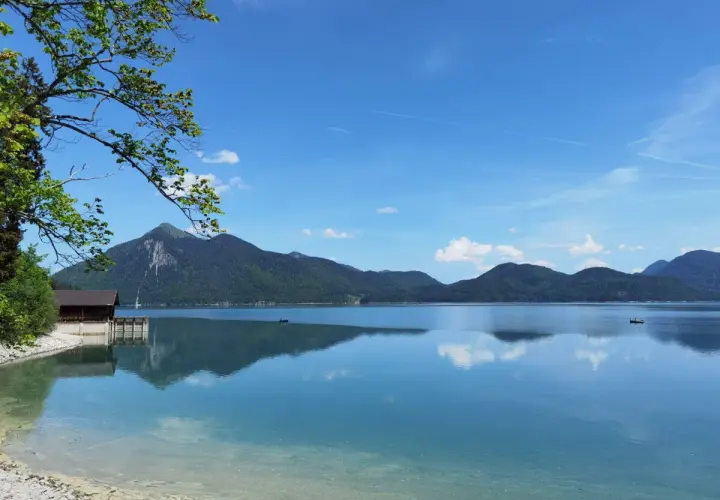 Karibik-Feeling am Walchensee: Ein Boot gleitet über das spiegelglatte Wasser, Berge im Hintergrund laden zum Baden ein.