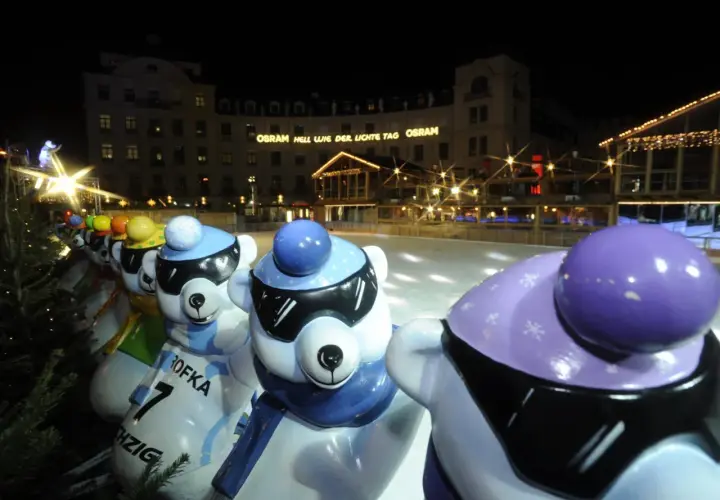Bunte Eisbären-Figuren am Stachus Weihnachtsmarkt in München, mit Lichtern und einer Eisbahn im Hintergrund.