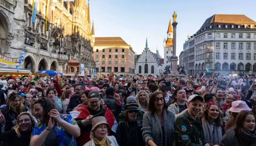 Bunte Menge feiert ausgelassen Fasching am Marienplatz in München. Menschen in Kostümen jubeln und tanzen vor historischer Kulisse.