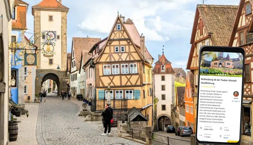 Romantische Gassen und Fachwerkhäuser in Rothenburg ob der Tauber. Ein Smartphone zeigt eine Stadtführung an.