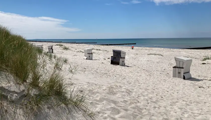 Hiddensee Strand mit Strandkörben und Dünen. Das Meer glänzt in der Sonne, ein einsamer Mensch spielt im Sand.