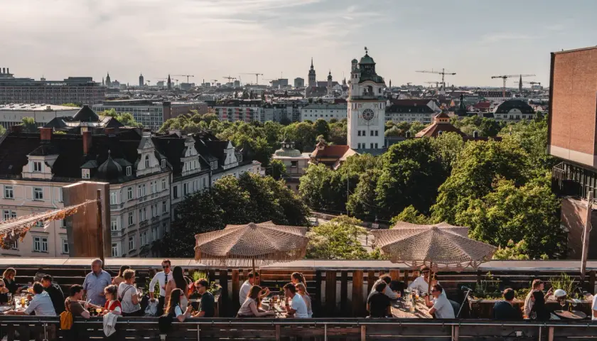 Menschen genießen das Leben auf einem **rooftop Munich** mit Blick auf die Stadt und den Turm.