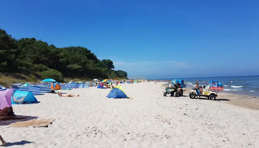 Sonniger Strandtag in Nonnewitz an der Ostsee. Menschen entspannen unter bunten Zelten, während Strandverkäufer Eis und Getränke anbieten.