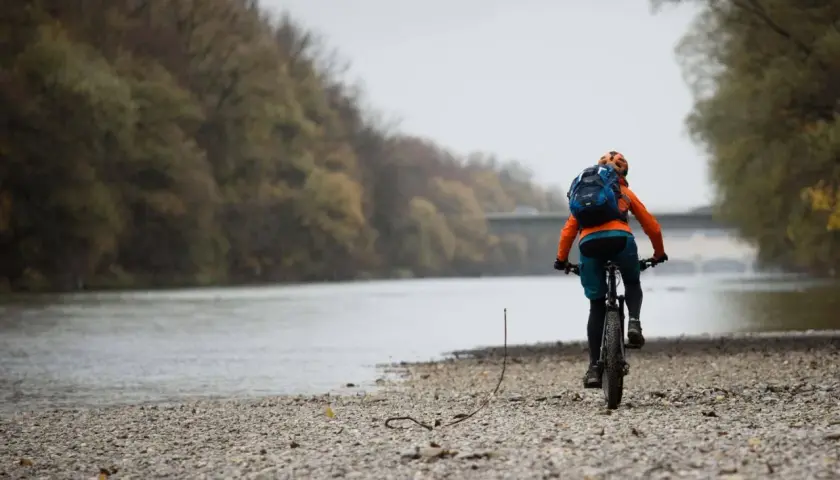 Radfahrer auf den Isar Trails, mit Rucksack und Helm, fährt am Flussufer entlang.