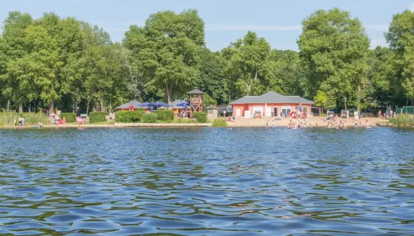 Sommerfreude an einem der **besten Badeseen Berlins**: Menschen planschen im Wasser, entspannen am Sandstrand und genießen die Sonne.