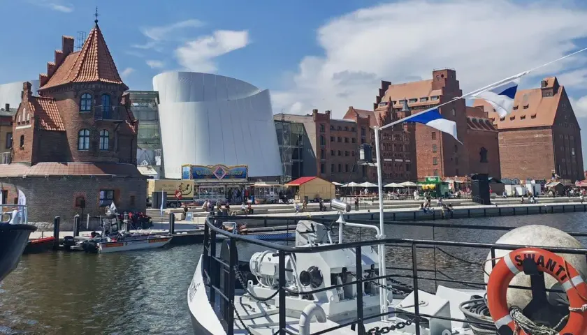 Hafenansicht mit historischer Backsteinarchitektur und modernem Gebäude. Ein Schiff mit Rettungsring liegt im Vordergrund. Stralsund sehenswertes Panorama.