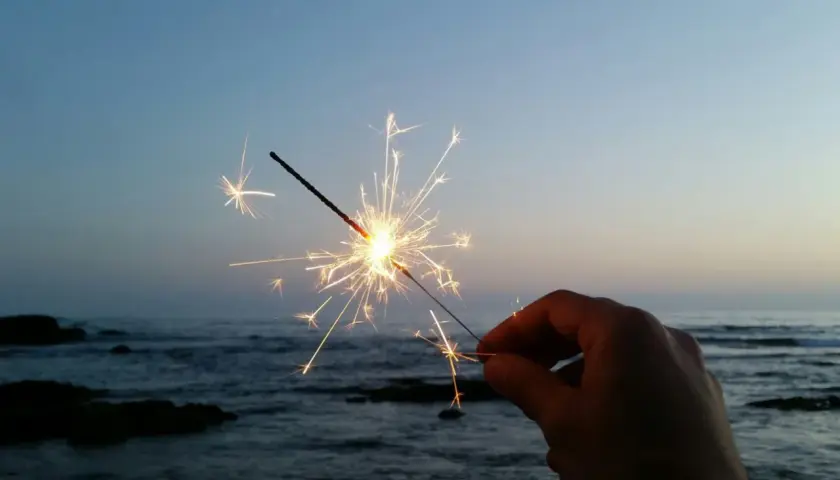 Ein Wunderkerze leuchtet am Silvesterabend am Strand. Die Funken tanzen über dem ruhigen Meer und dem klaren Himmel.