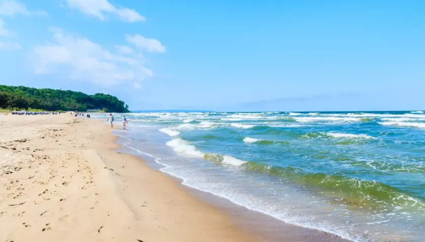 Ein sonniger Tag am Ostseebad Baabe. Menschen spazieren am breiten Sandstrand entlang, während die Wellen der Ostsee sanft ans Ufer rollen.