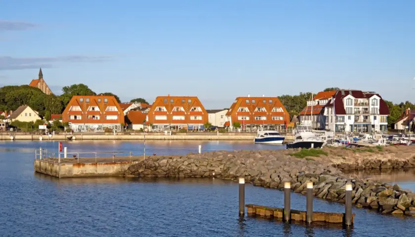 Hafen mit roten Ziegeldächern, Booten und einem Kirchturm im Hintergrund.