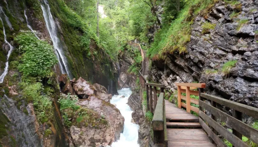 Holzstege führen durch die Klamm Berchtesgaden, vorbei an tosendem Wasser und moosbewachsenen Felsen.