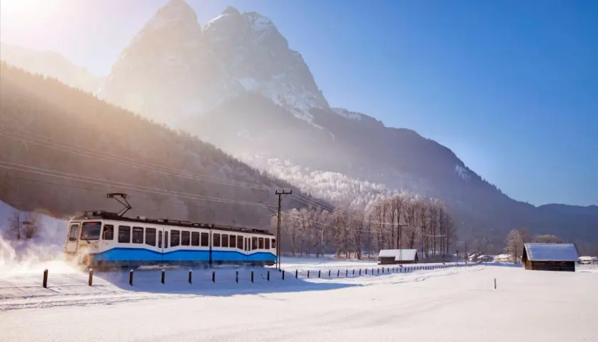 Blauer Zug fährt durch verschneite Alpenlandschaft, tolle Winterurlaub Ideen für Ihre Reise.