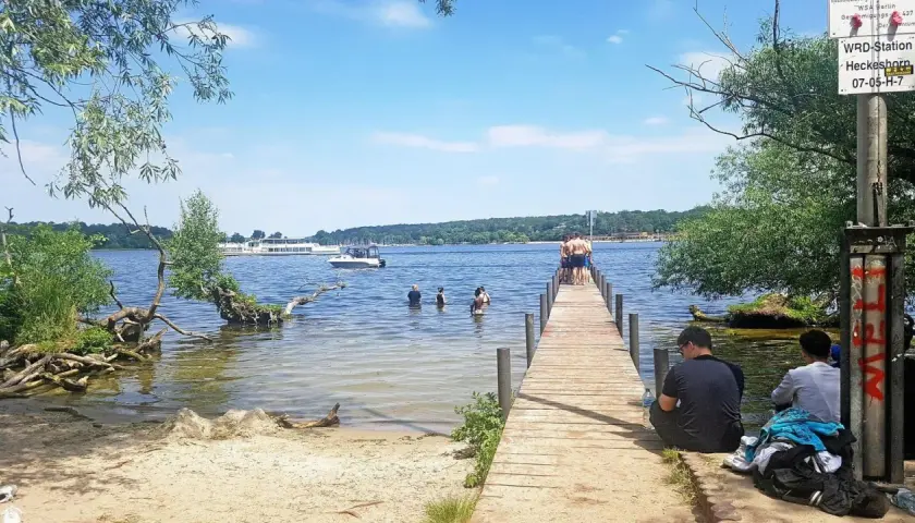 Sommer am ummanz strand: Menschen planschen im Wasser, andere sitzen am Steg. Ein sonniger Tag am See.
