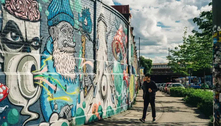 Mann geht an bunter Street Art in München vorbei. Die Wand ist mit fantasievollen Figuren und Mustern bemalt.