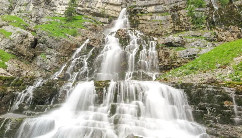 Ein beeindruckender, mehrstufiger murnau wasserfall stürzt über moosbewachsene Felsen in die Tiefe, umgeben von steilen, grünen Hängen.