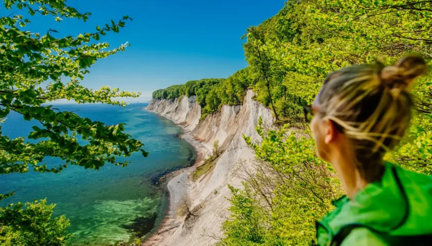 Frau blickt auf Kreidefelsen im Nationalpark Jasmund. Türkisfarbenes Meer und grüne Bäume.