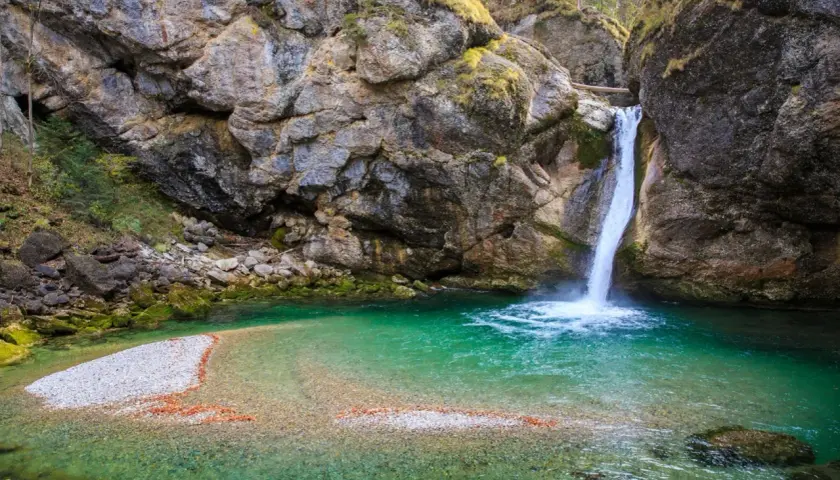 Türkiser bergsee mit einem tosenden wasserfall, der in die klare Tiefe stürzt. Felsen und Moos umrahmen dieses Naturschauspiel.