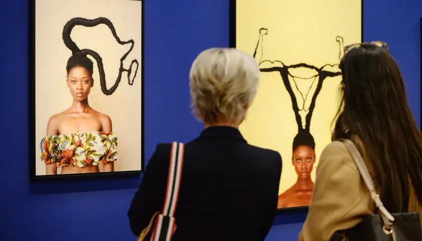 Besucher betrachten Kunstwerke bei der ausstellung hypo kunsthalle. Ein Bild zeigt eine Frau mit afrikanisch geformten Haaren, das andere eine Frau mit Gebärmutter-Frisur.