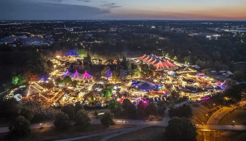 Nachtansicht des beleuchteten Tollwood Festivals im Olympiapark München mit bunten Zelten und Lichtern.