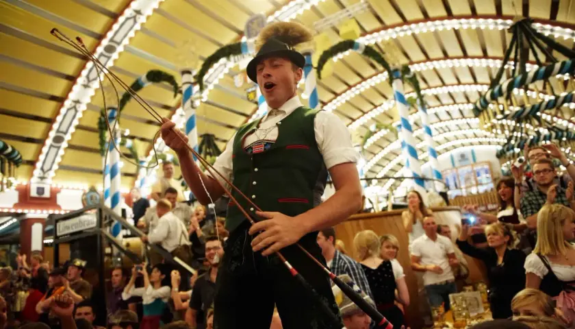 Mann im bierzelt oktoberfest mit Peitsche, jubelnde Menge im Hintergrund.