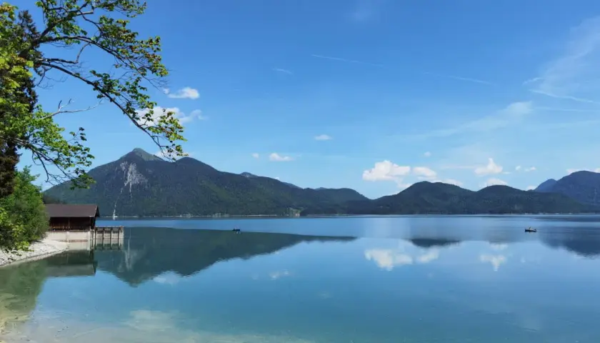 Karibik-Feeling am Walchensee: Ein Boot gleitet über das spiegelglatte Wasser, Berge im Hintergrund laden zum Baden ein.