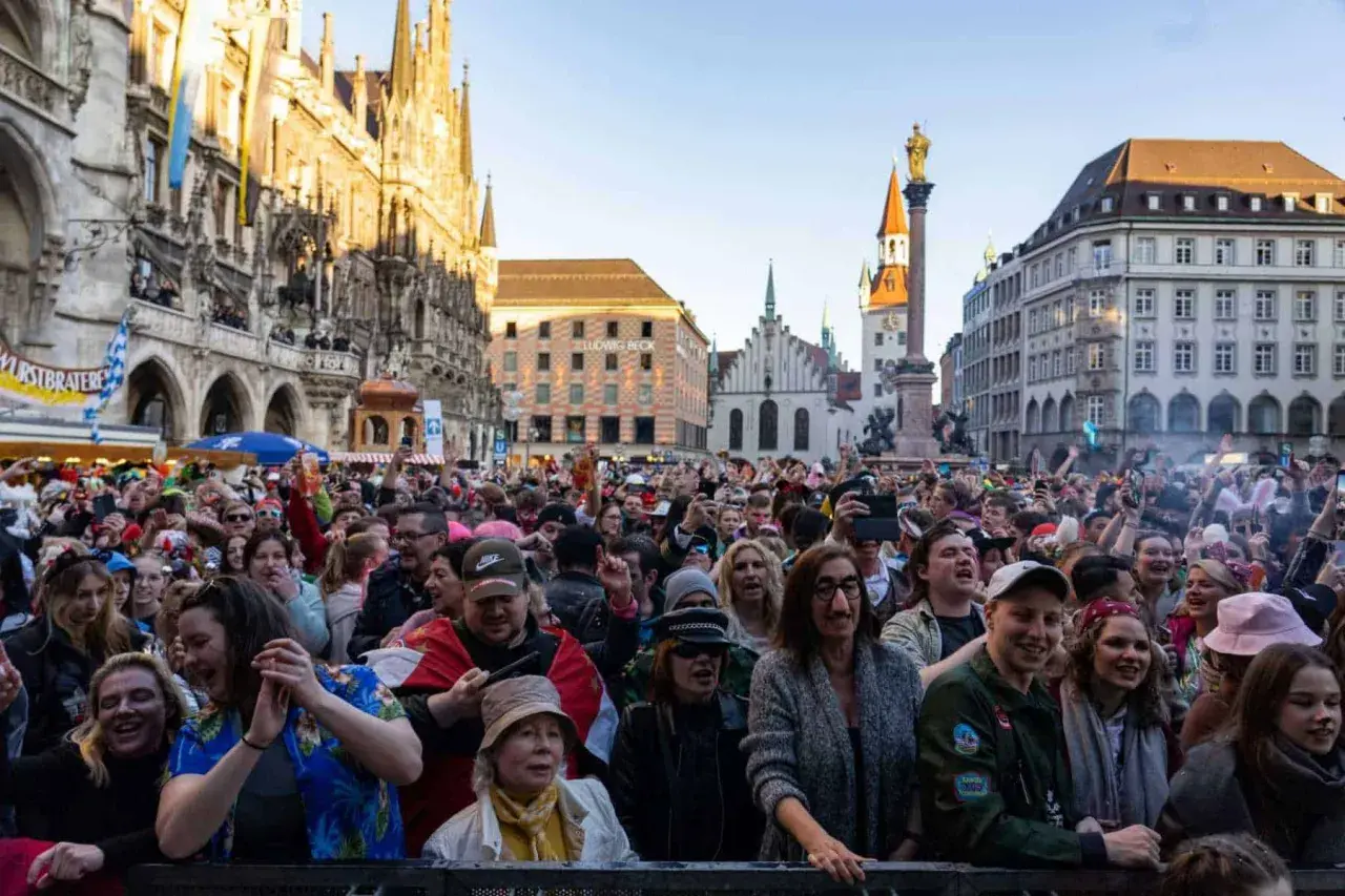 Bunte Menge feiert ausgelassen Fasching am Marienplatz in München. Menschen in Kostümen jubeln und tanzen vor historischer Kulisse.