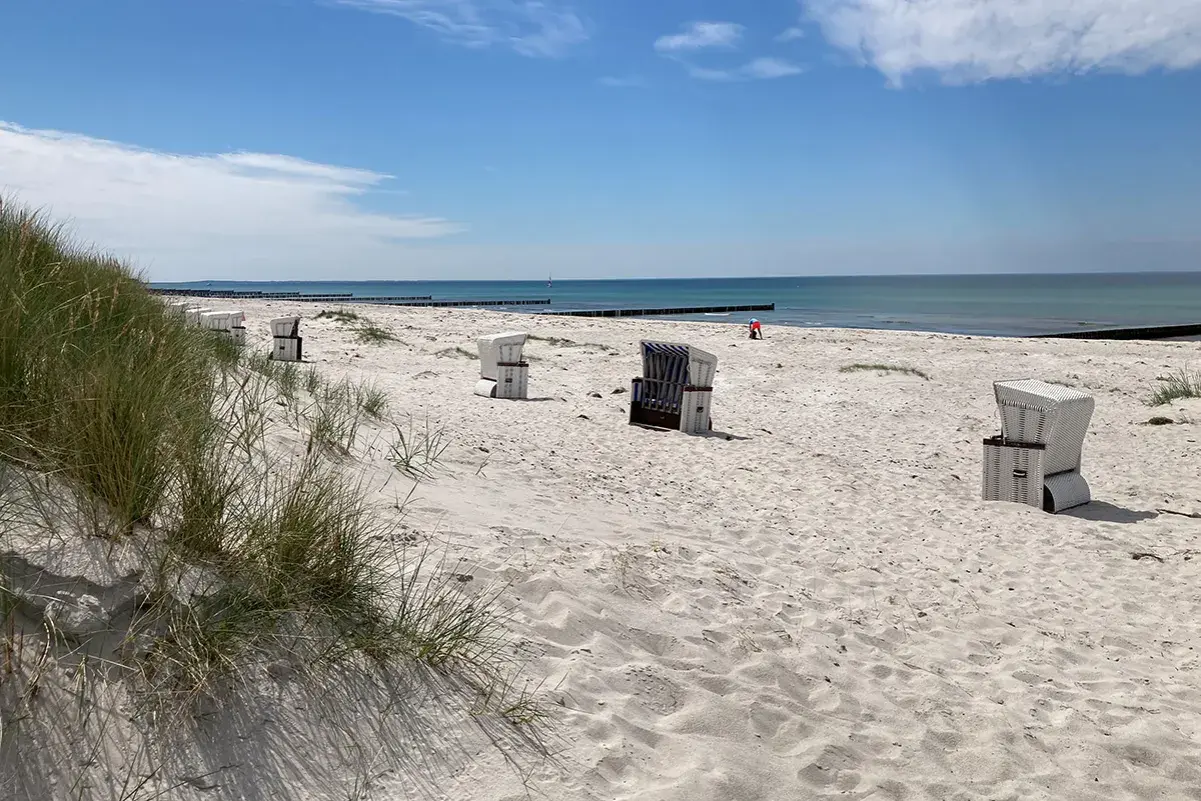 Hiddensee Strand mit Strandkörben und Dünen. Das Meer glänzt in der Sonne, ein einsamer Mensch spielt im Sand.