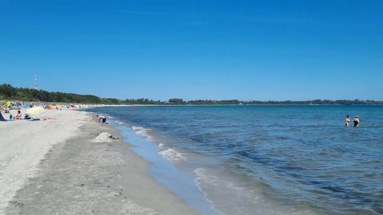 Sonniger Tag am Juliusruh Strand. Menschen entspannen sich am Sand, Kinder bauen Sandburgen, andere baden im ruhigen Meer.
