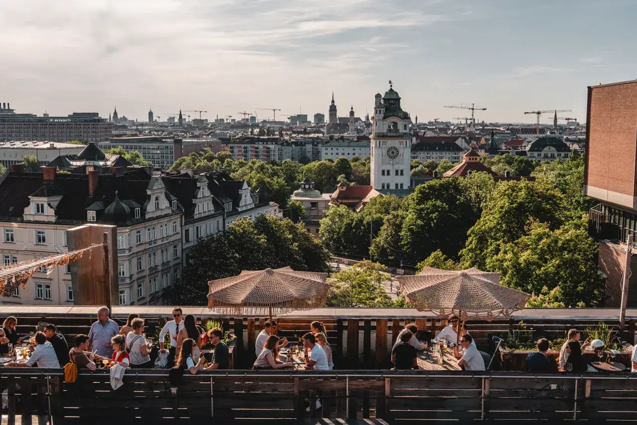 Menschen genießen das Leben auf einem **rooftop Munich** mit Blick auf die Stadt und den Turm.