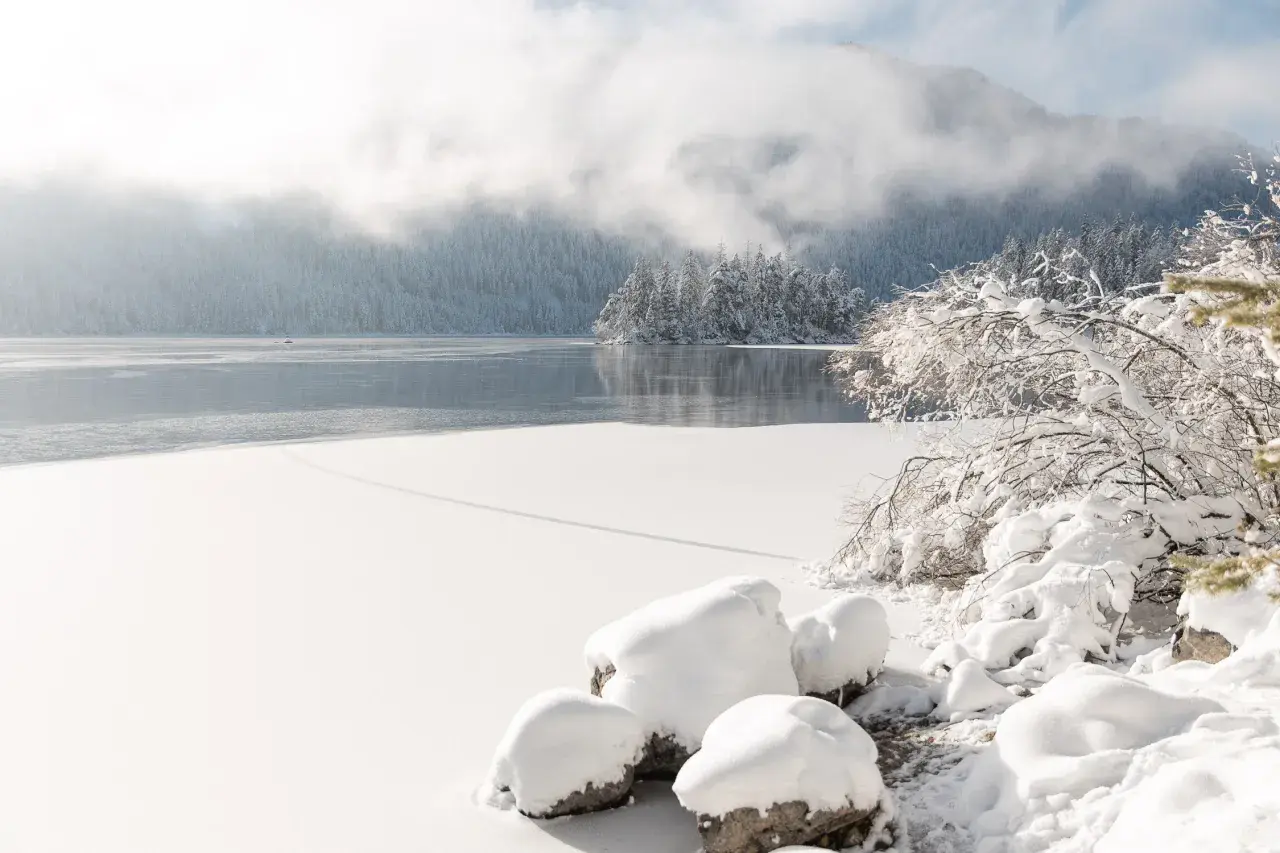 Eibsee winter: Eisbedeckter See, schneebedeckte Bäume und Berge im Nebel. Ein friedlicher Anblick.