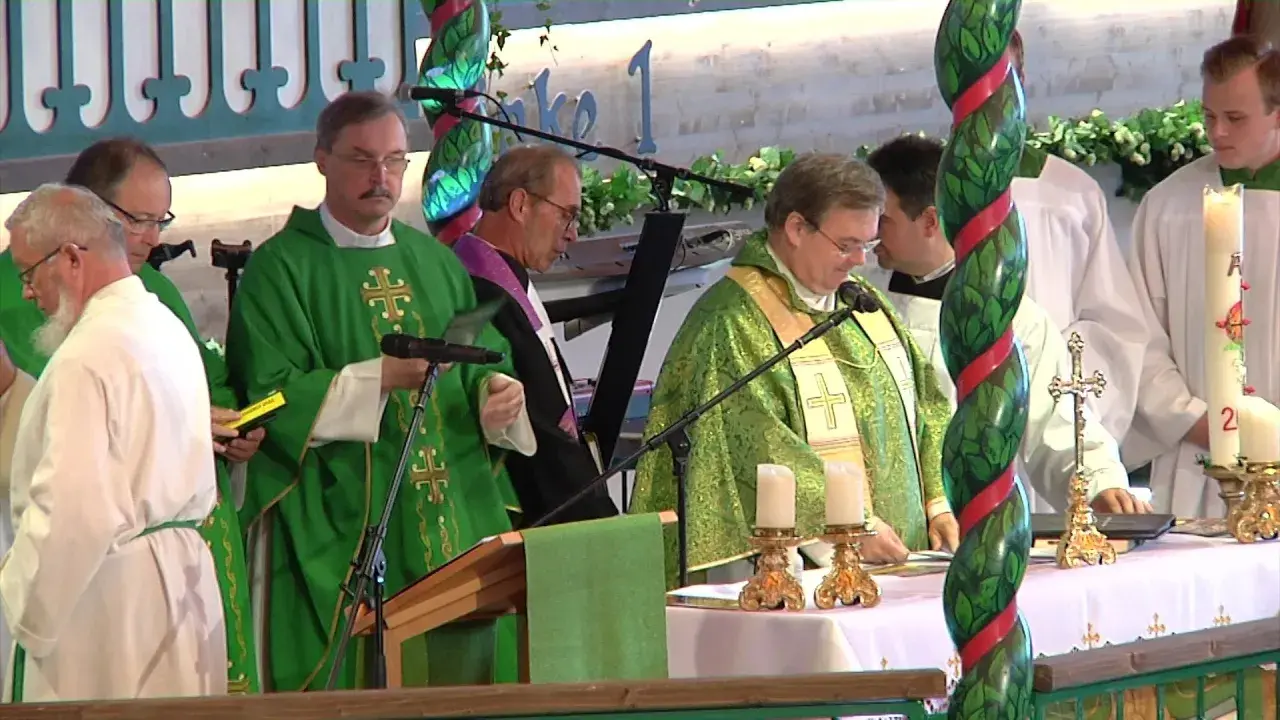 Priester in grünen Gewändern bei einem Gottesdienst in den Kirchen. Kerzen und ein Kreuz stehen auf dem Altar.