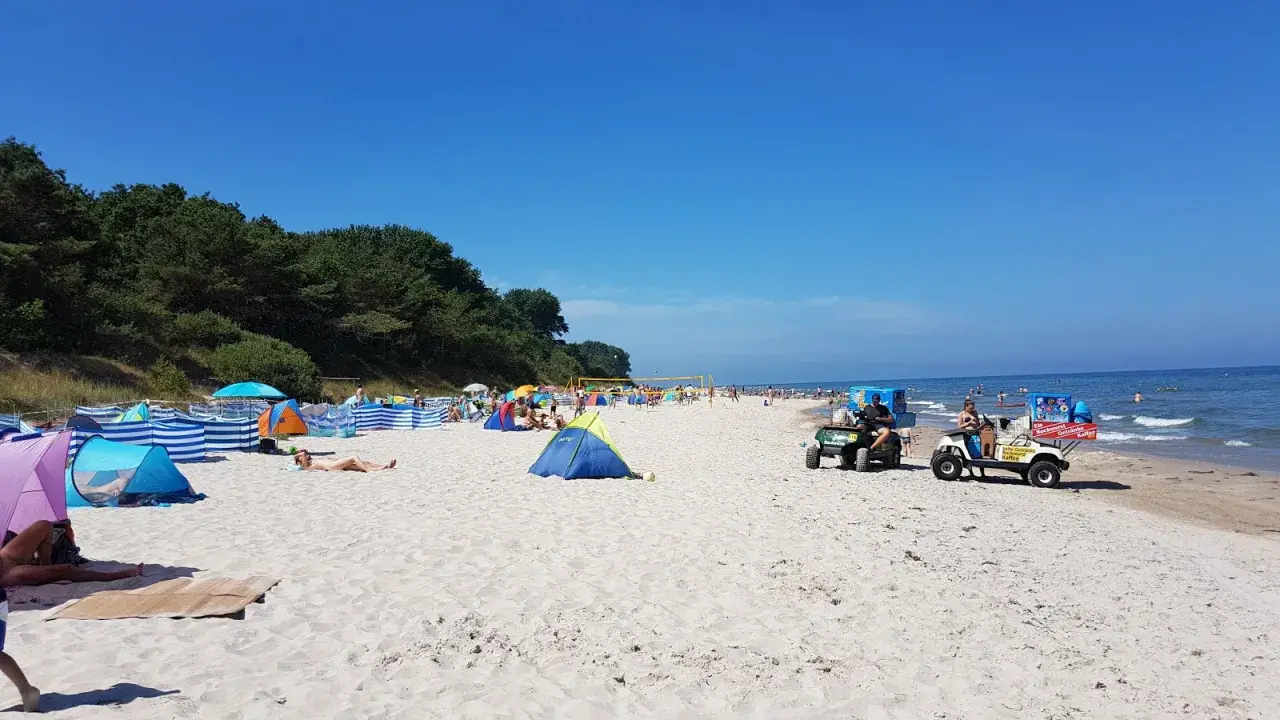Sonniger Strandtag in Nonnewitz an der Ostsee. Menschen entspannen unter bunten Zelten, während Strandverkäufer Eis und Getränke anbieten.