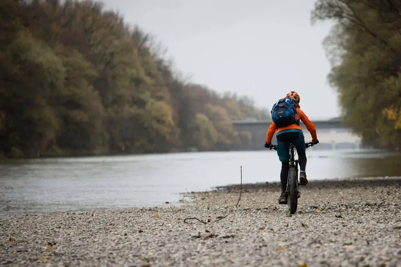 Radfahrer auf den Isar Trails, mit Rucksack und Helm, fährt am Flussufer entlang.