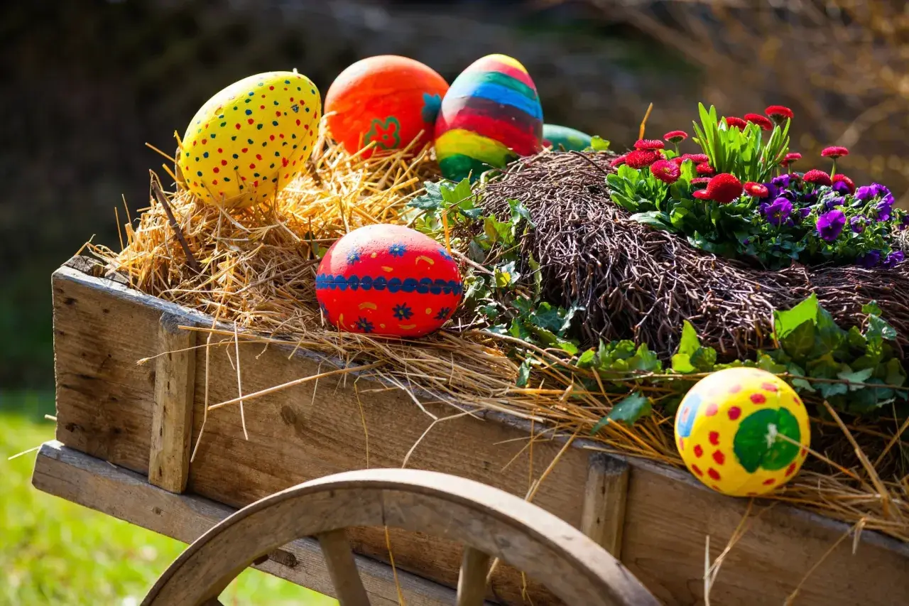 Bunte Ostereier und Blumen schmücken einen alten Wagen, perfekt für Ostermontag Veranstaltungen.